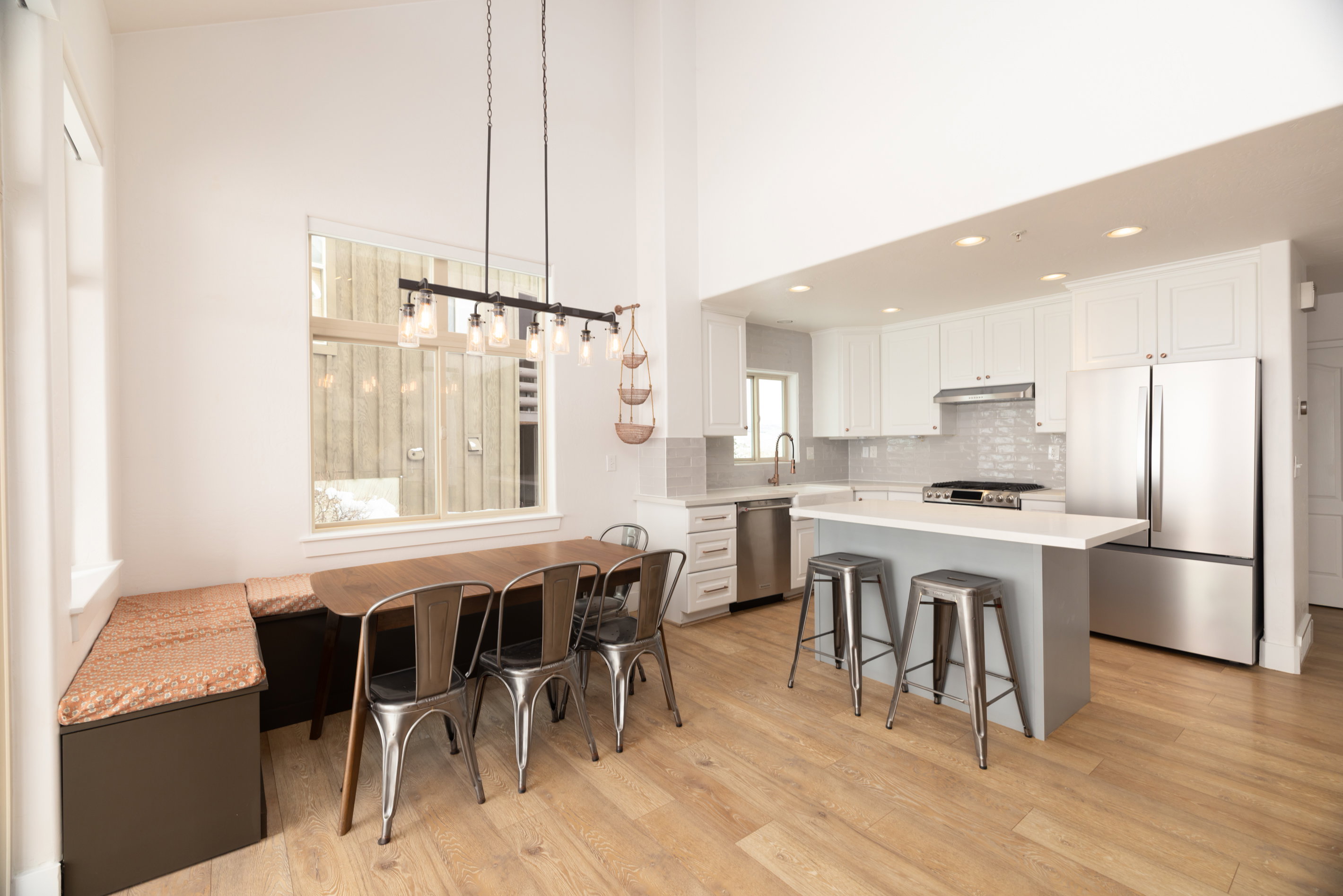 Open-concept kitchen and dining area featuring high vaulted ceilings, wood-finish flooring, white cabinetry, stainless steel appliances, and a kitchen island with seating