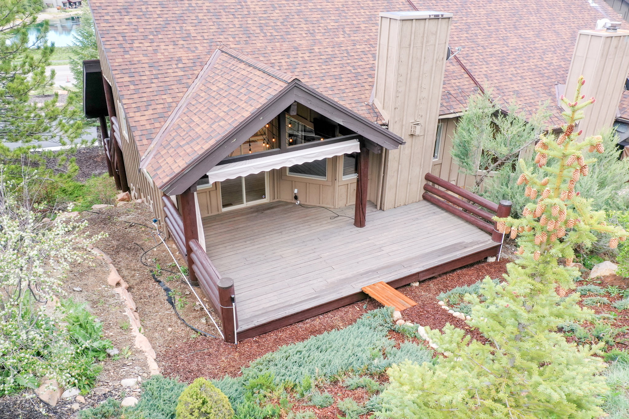 Expansive wood-finish deck with log-style railings, featuring a retractable awning and string lighting