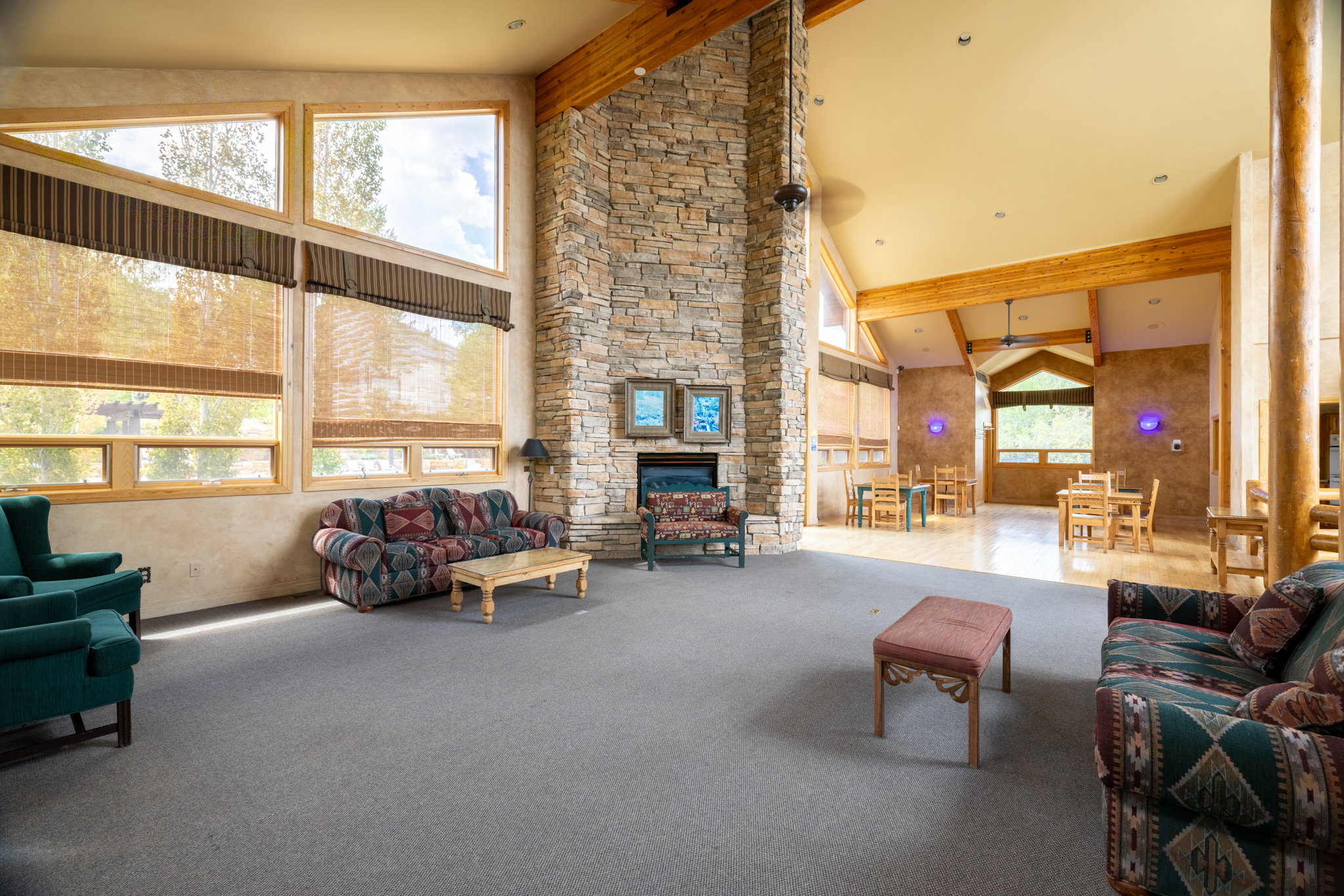 Spacious open-concept room featuring a prominent stone-clad fireplace and high vaulted ceilings with exposed wood beams