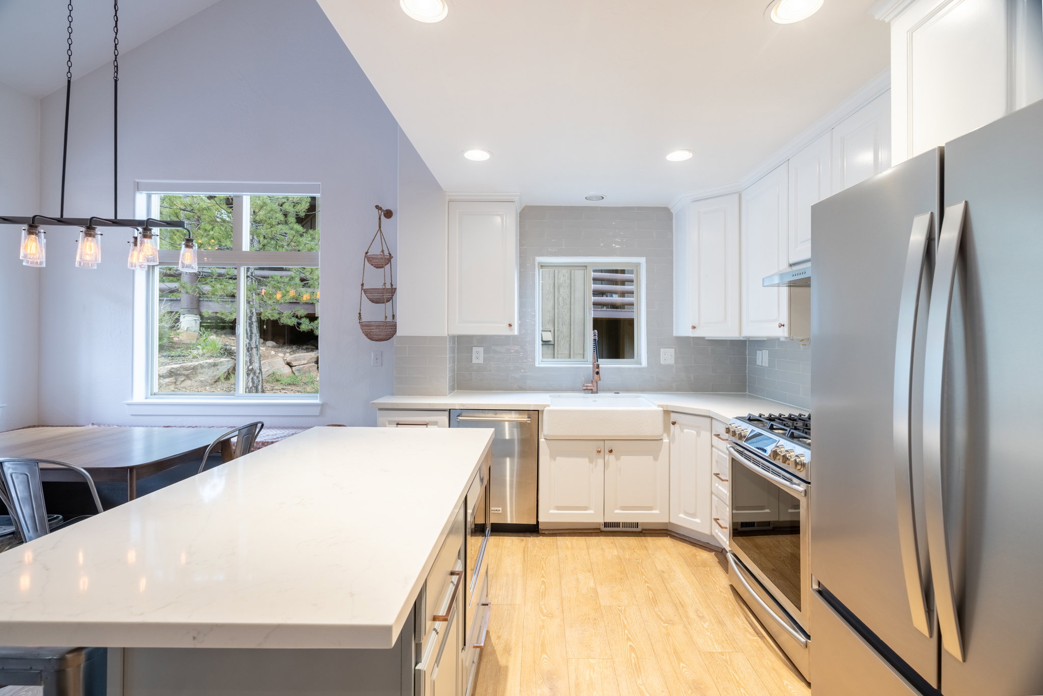 Open-concept kitchen featuring an expansive island with a light-toned countertop, white cabinetry, stainless steel appliances, a farmhouse-style sink, and light wood-finish flooring