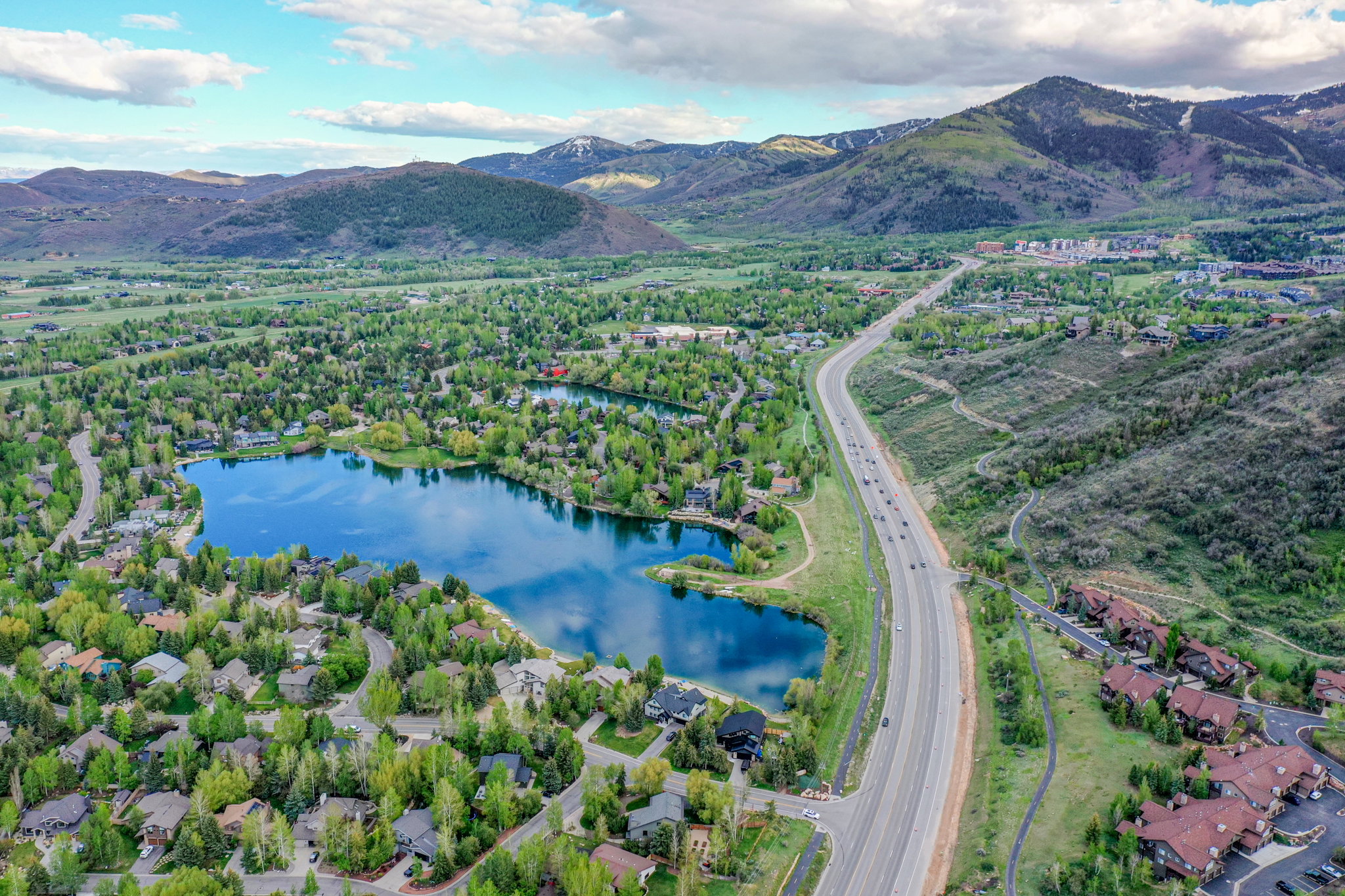 Expansive natural landscape featuring a prominent lake surrounded by residential properties, a multi-lane highway, and distant mountains with snow-capped peaks