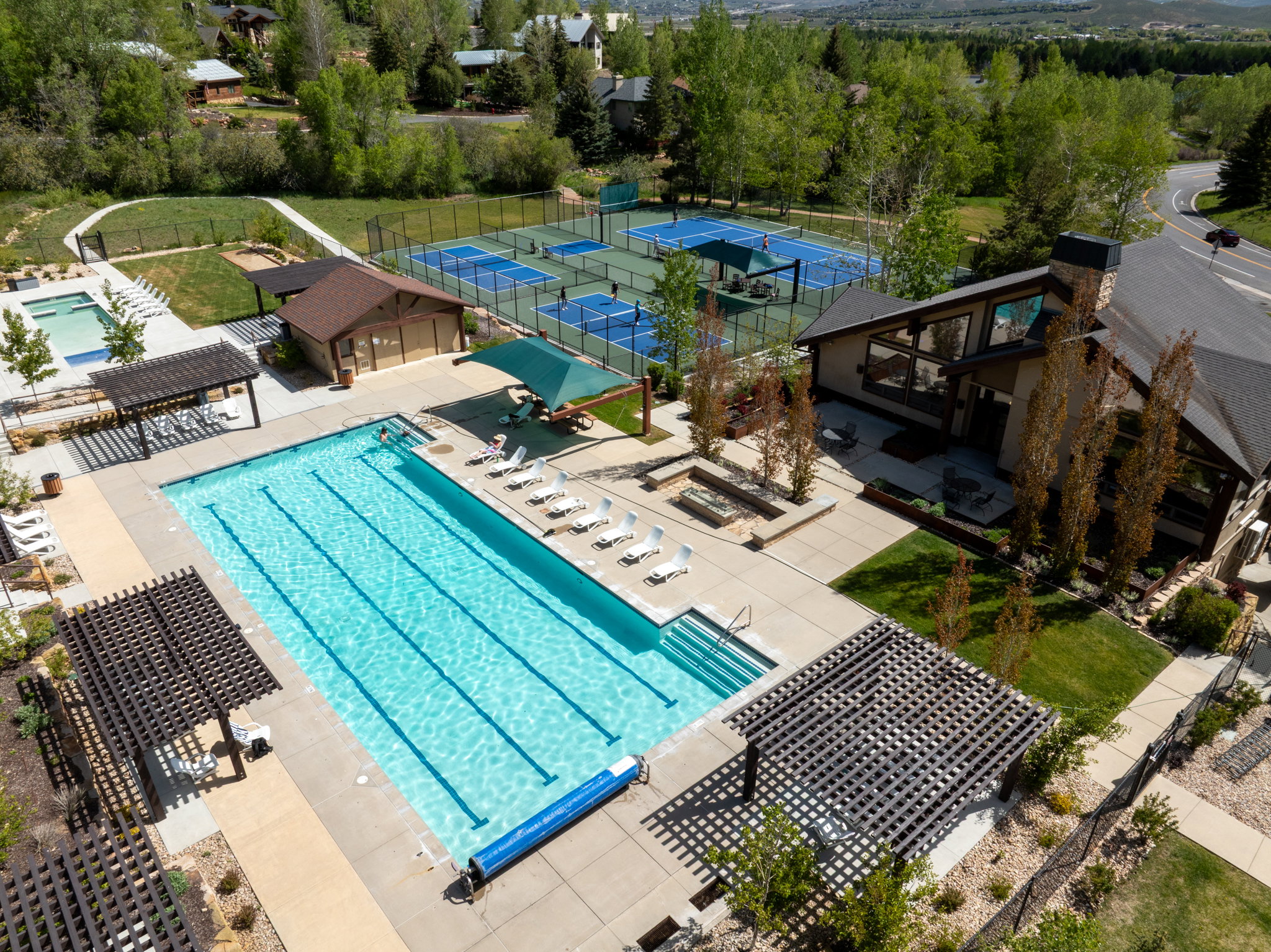 Expansive outdoor recreational area featuring a multi-lane swimming pool, multiple pergolas, a separate children's pool, and multiple tennis courts