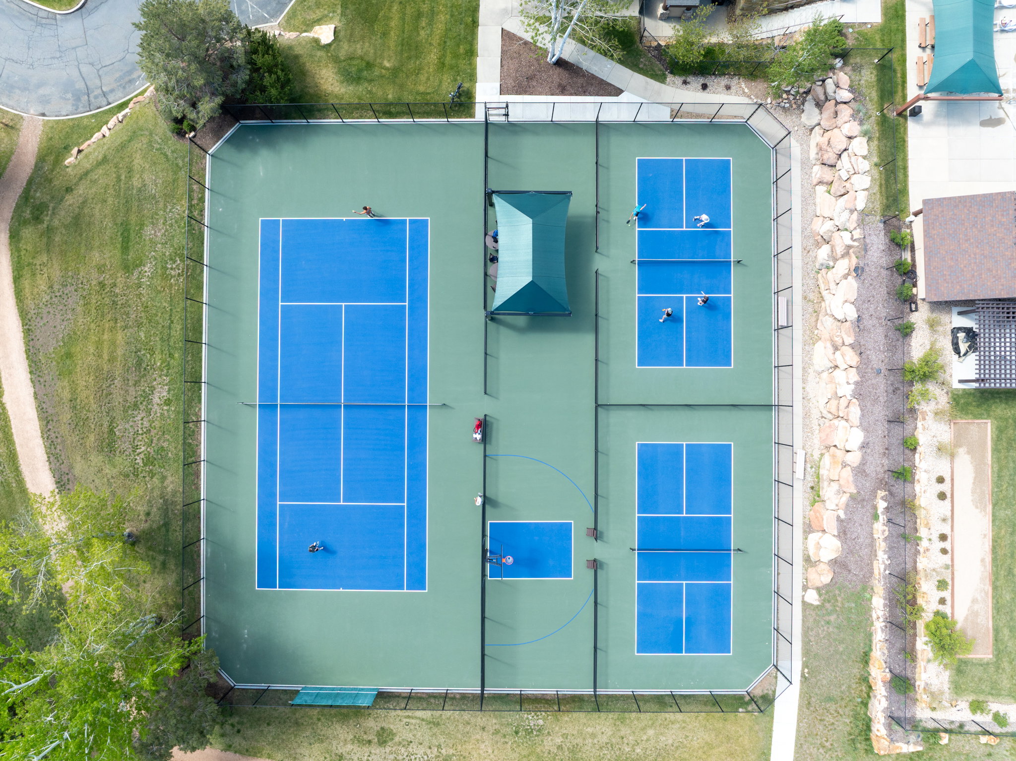 Tennis and pickleball courts with perimeter fencing and a shaded seating area