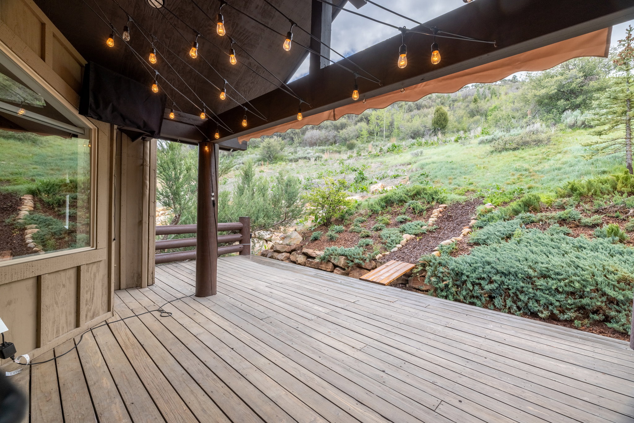 Expansive outdoor deck featuring wood-finish flooring, string lights, and an awning