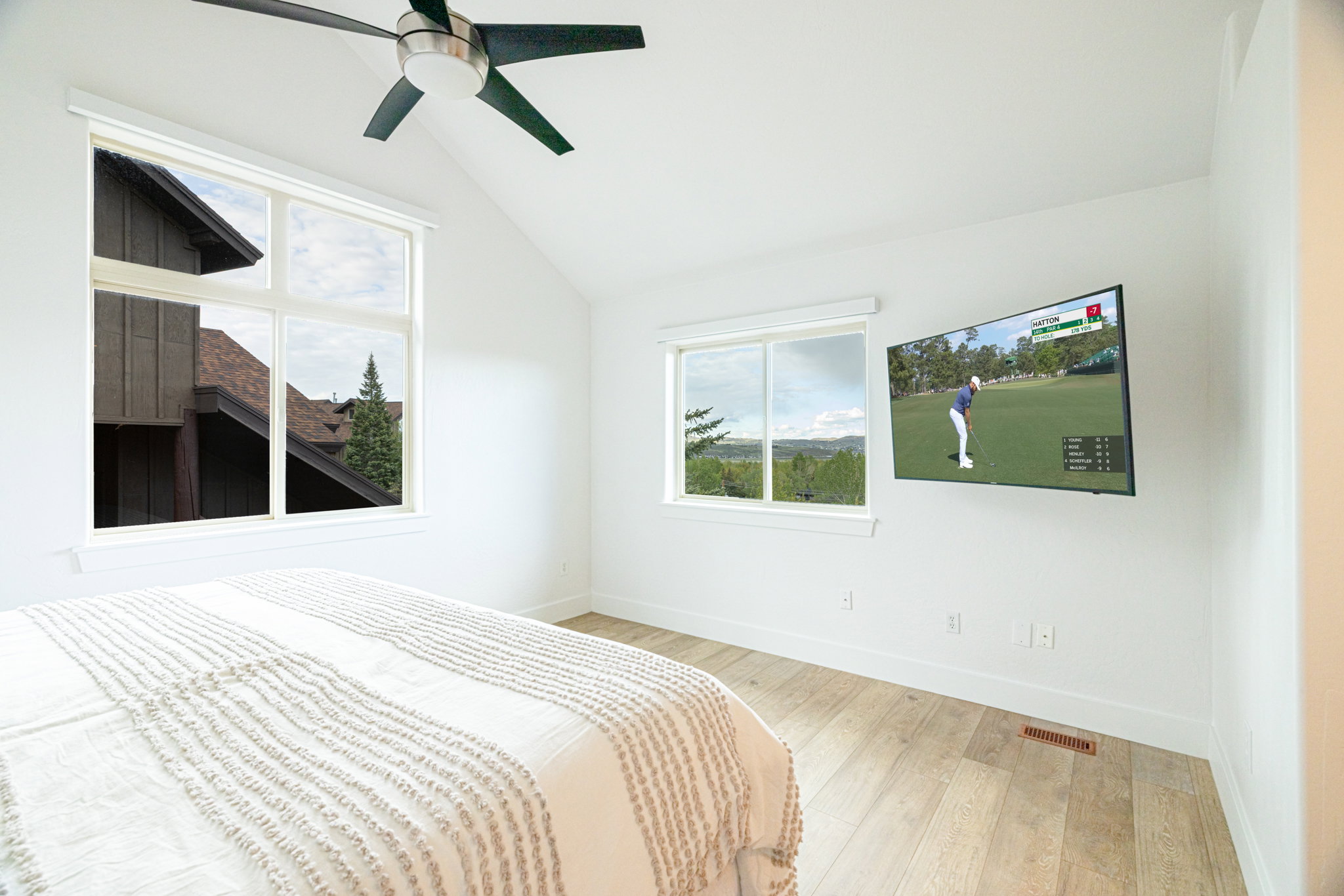 Vaulted ceiling room featuring light wood-finish flooring, two large windows, and a ceiling fan with integrated lighting