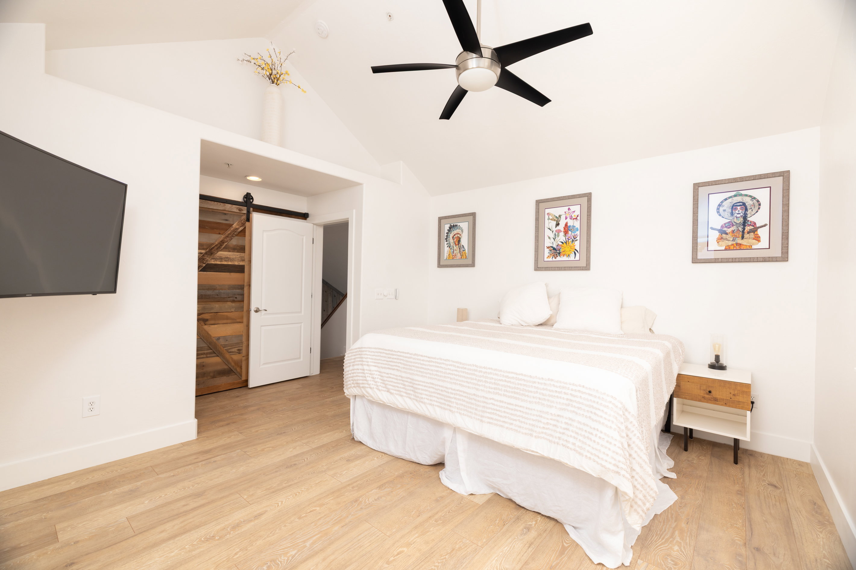 Vaulted ceiling with a black ceiling fan, wood-finish flooring, and a rustic wood barn door