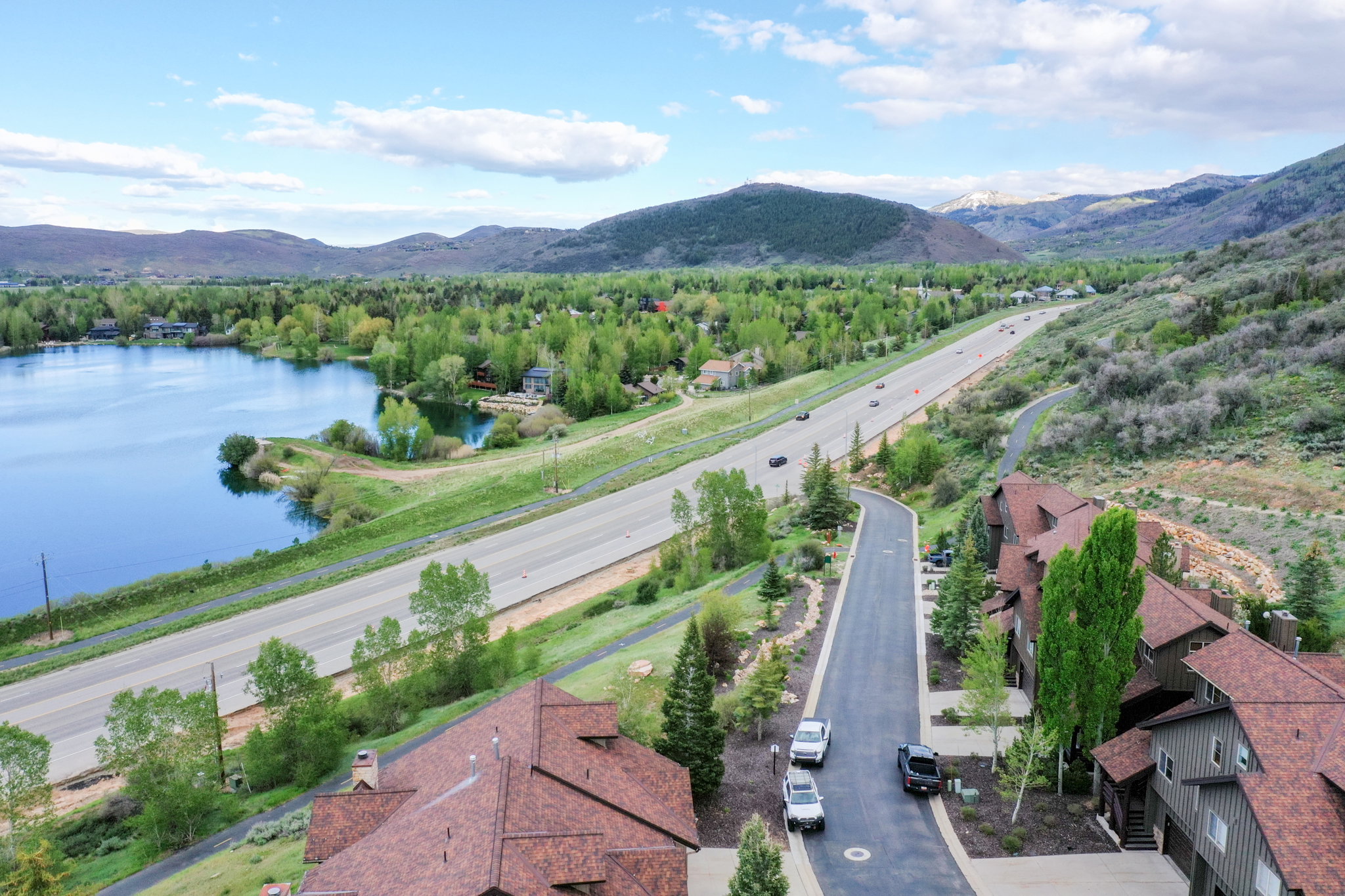 Aerial perspective showcasing a lake, highway, and residential buildings with surrounding natural landscape