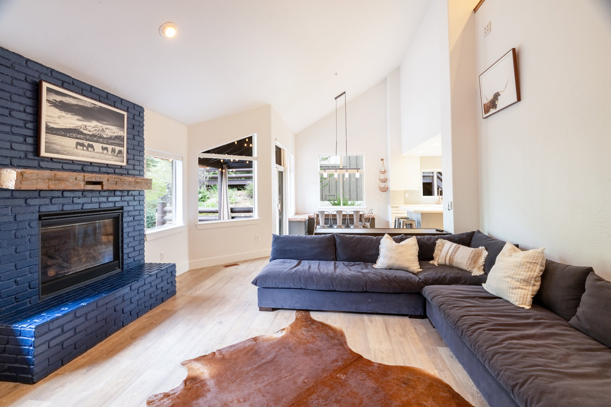 Spacious living area featuring a blue brick fireplace with a wood mantel, light wood-finish flooring, and high vaulted ceilings