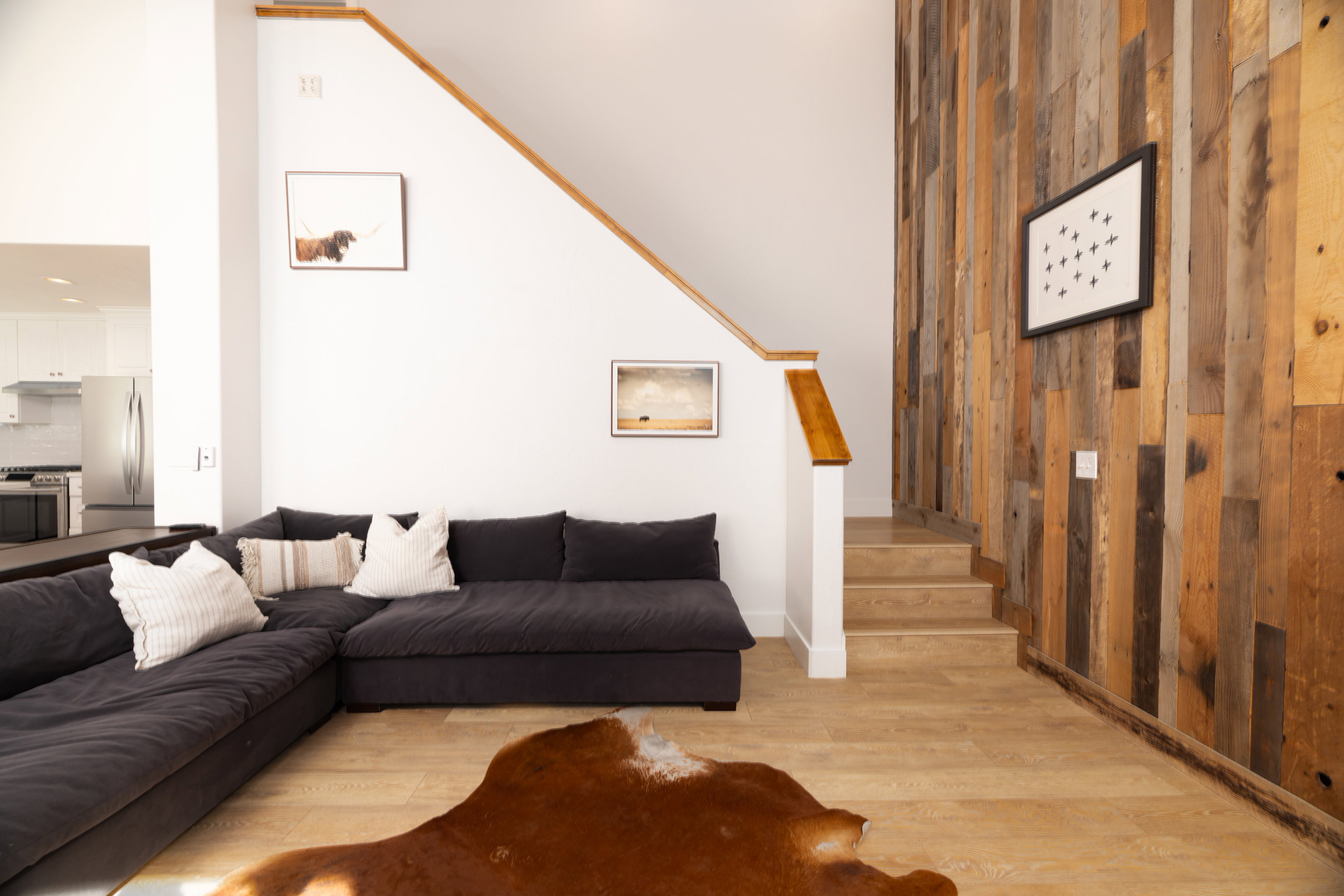 Living area featuring a vertical wood plank accent wall, wood-finish flooring, and a white staircase with a natural wood handrail
