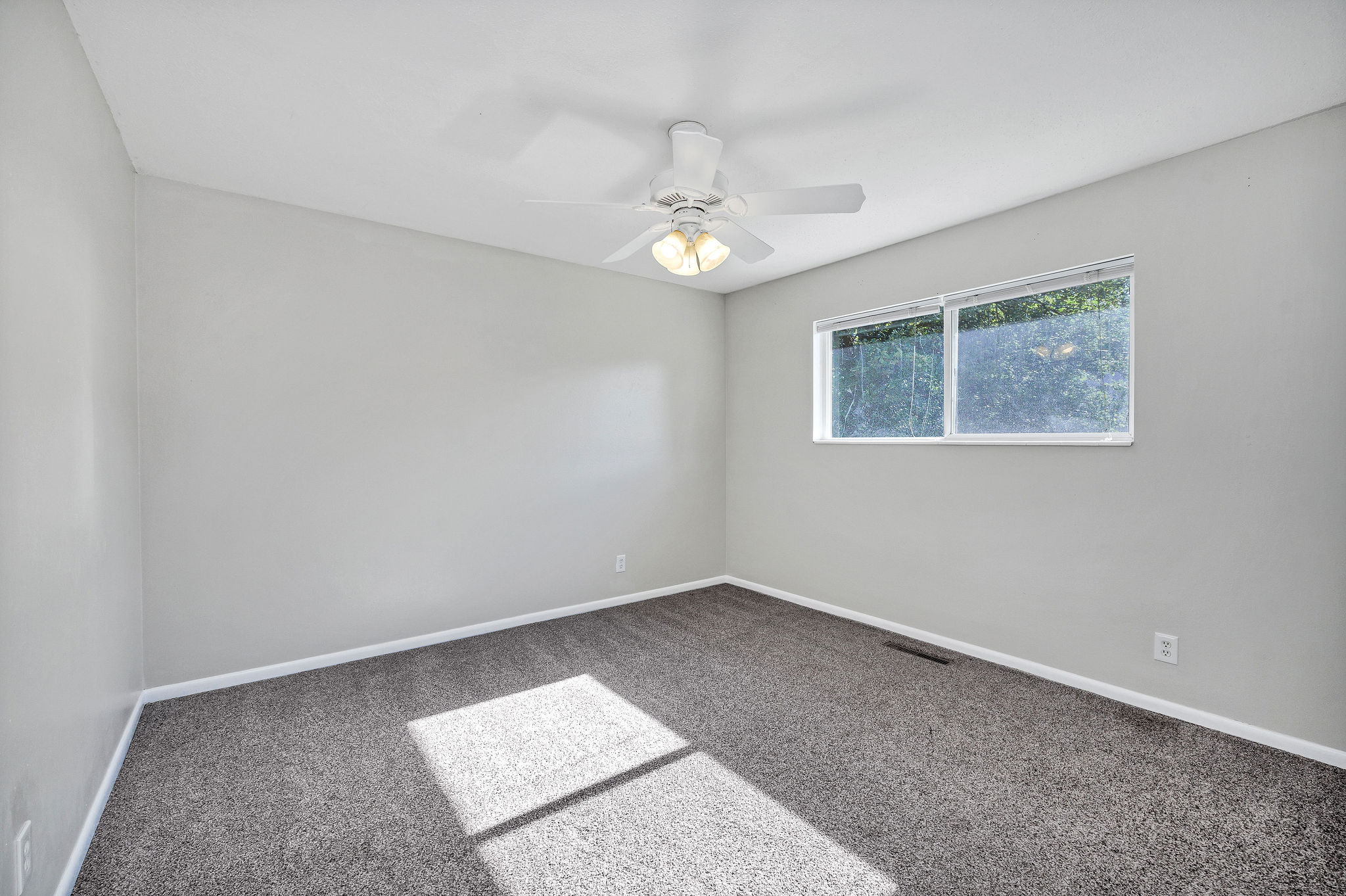 Carpeted interior space featuring light gray wall paint, white trim, and a ceiling fan with integrated lighting