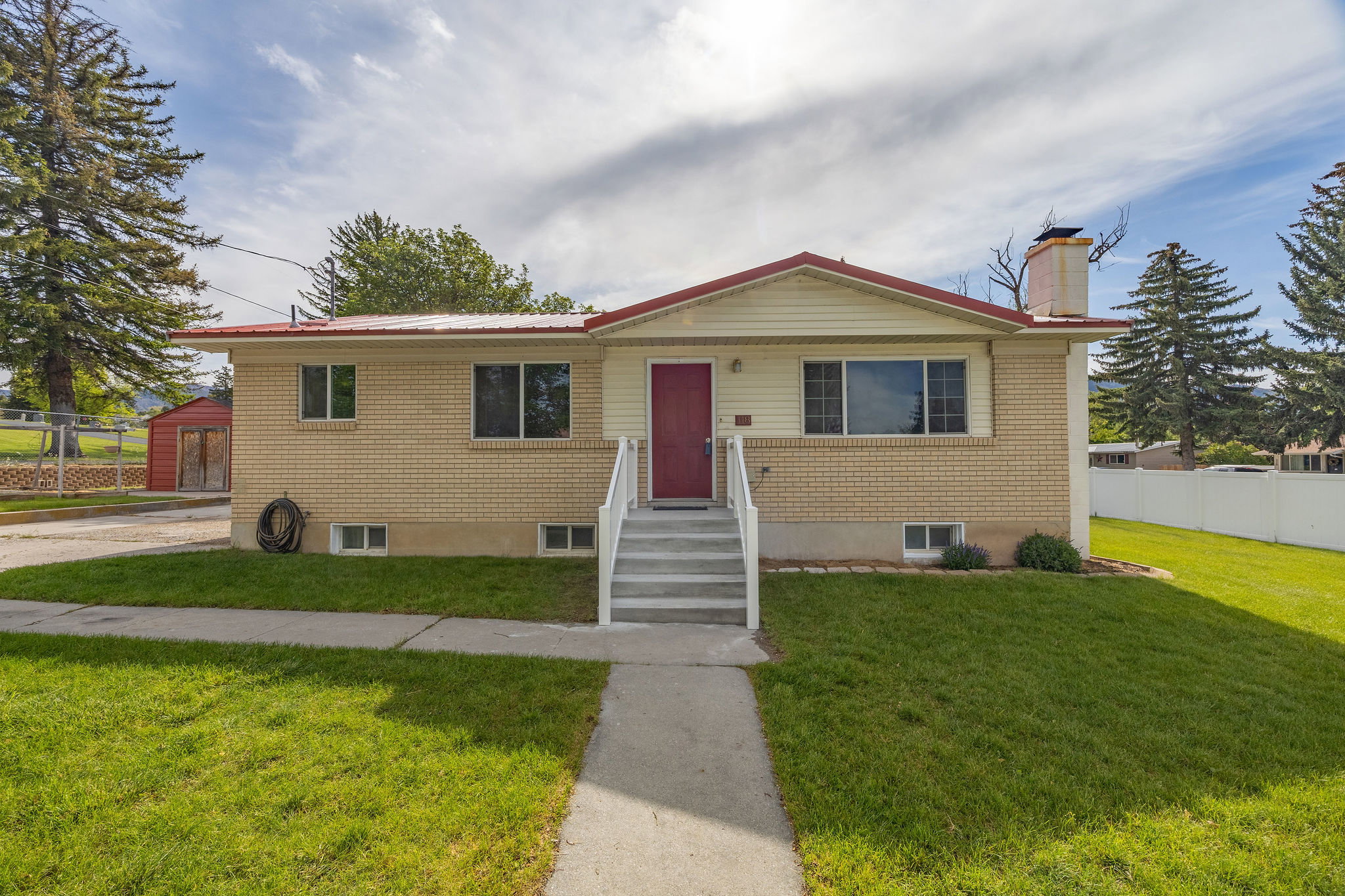 Split-level residence featuring a brick and siding exterior, red metal roof, and a prominent red entry door