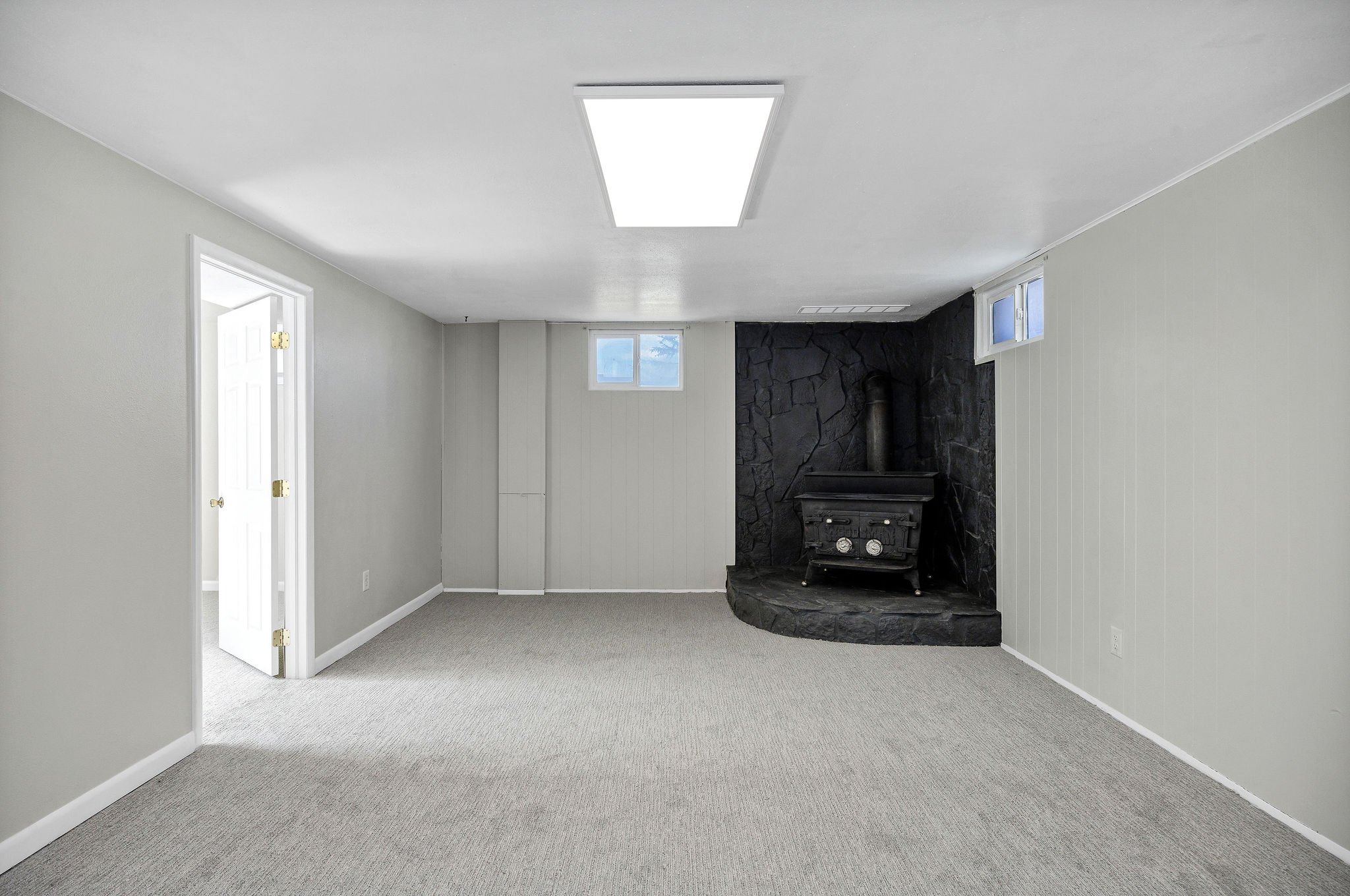 Spacious room featuring a corner wood-burning stove with a stone hearth, light gray walls, light gray carpeting, and a recessed ceiling light fixture