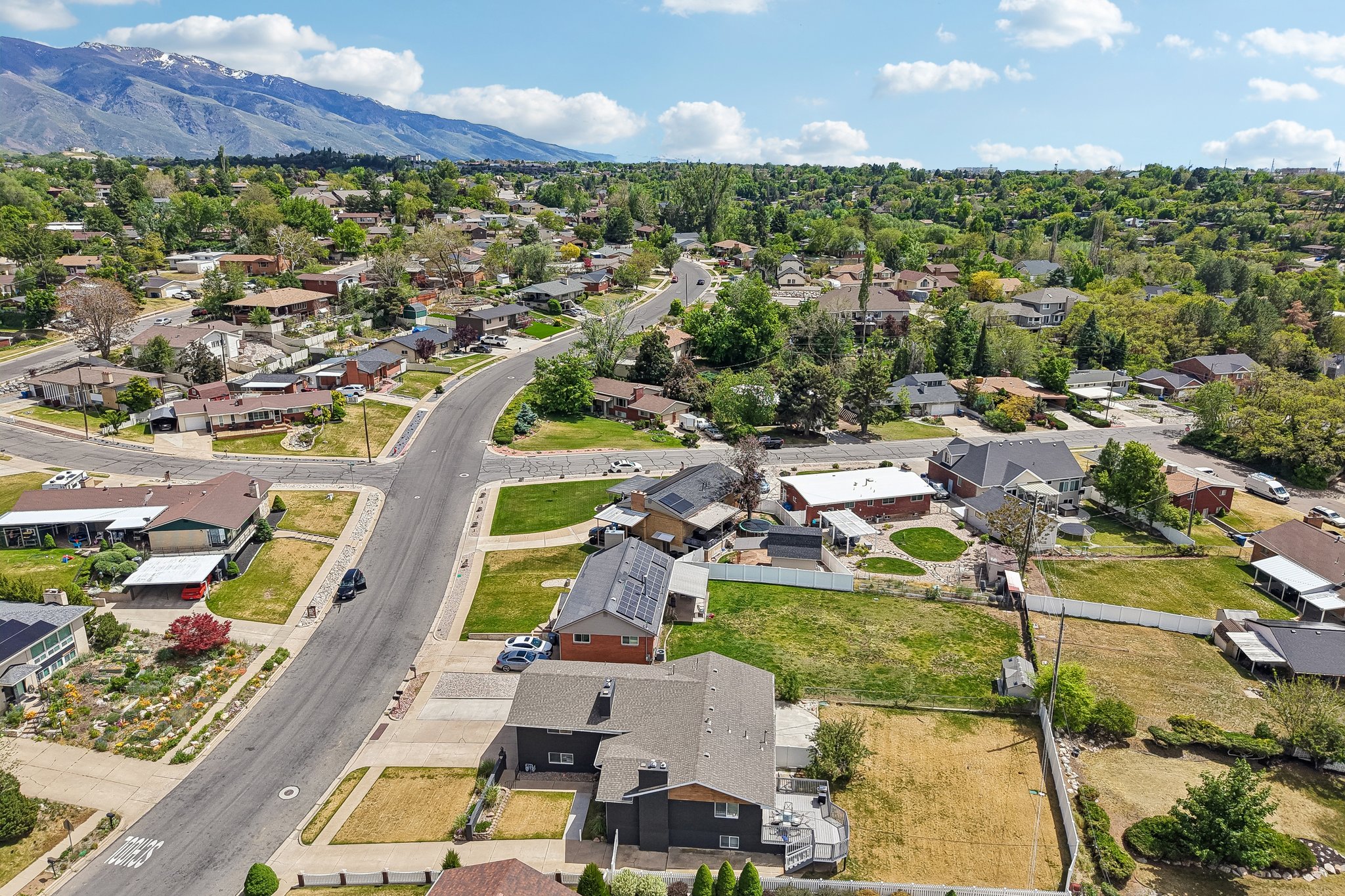 Residential neighborhood with mature trees, paved streets, and mountain backdrop