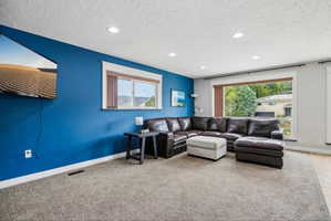 Carpeted living area featuring a large picture window, a secondary window, recessed lighting, and a blue accent wall