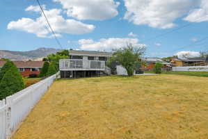 Expansive backyard featuring a white picket fence, a multi-level deck with white railings, a concrete patio, and a mature tree