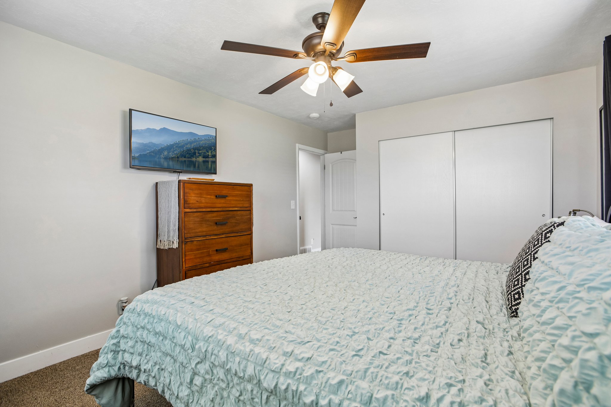 Spacious room featuring a ceiling fan with integrated lighting, wall-mounted television, and light-toned walls