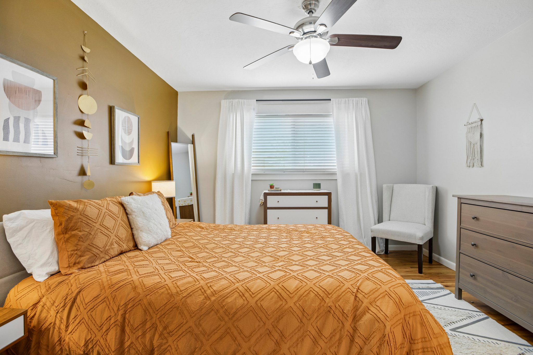 Bedroom featuring a ceiling fan with integrated lighting, a window with blinds and sheer drapes, and wood-finish flooring