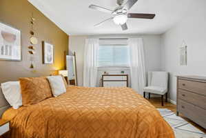 Bedroom featuring a ceiling fan with integrated lighting, a window with blinds and sheer drapes, and wood-finish flooring
