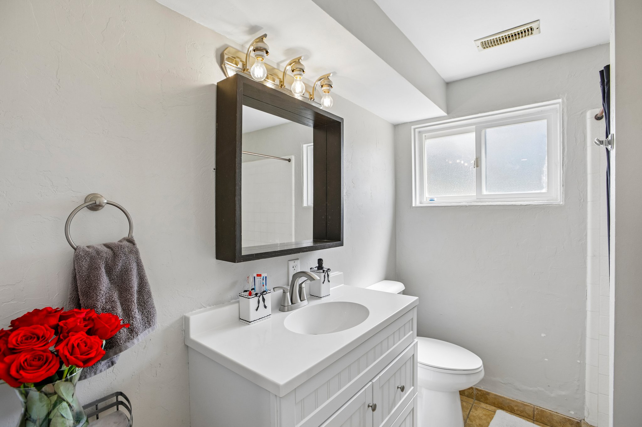 Bathroom featuring a white vanity with an integrated sink, brushed nickel faucet, and a coordinating mirror with overhead lighting