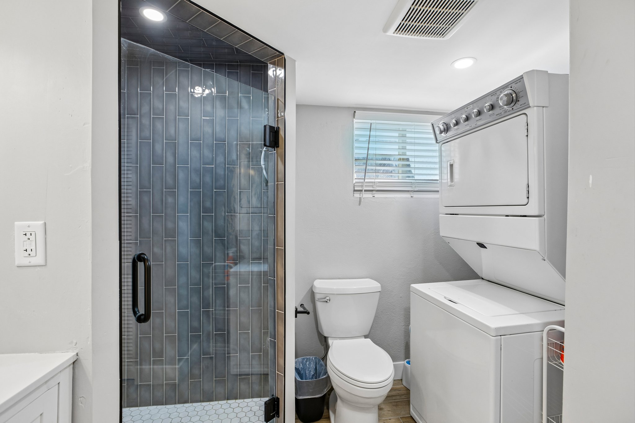 Bathroom featuring a glass-enclosed shower with subway tile, white hex tile flooring, and a stacked washer and dryer