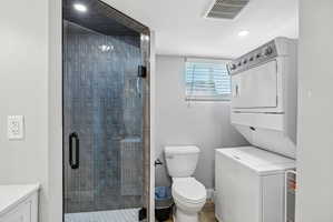 Bathroom featuring a glass-enclosed shower with subway tile, white hex tile flooring, and a stacked washer and dryer