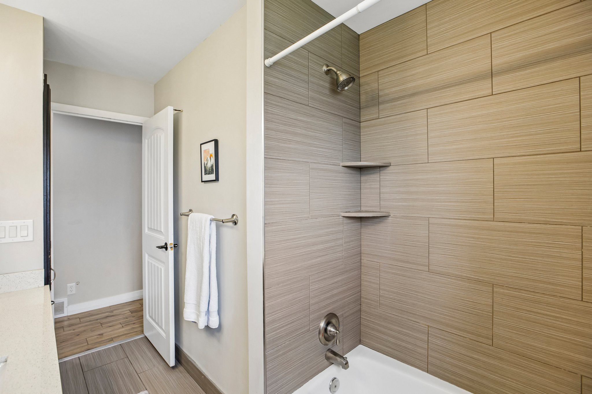 Bathtub with subway tile surround featuring integrated corner shelving, a bronze finish showerhead, and a chrome-finish faucet