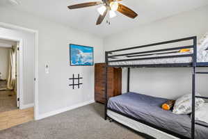 Carpeted room with light gray walls, a ceiling fan, and a doorway opening to an adjacent space with wood-finish flooring