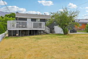 Rear exterior showcasing a spacious elevated deck with white railing, a mature shade tree, a concrete patio, and a white privacy fence