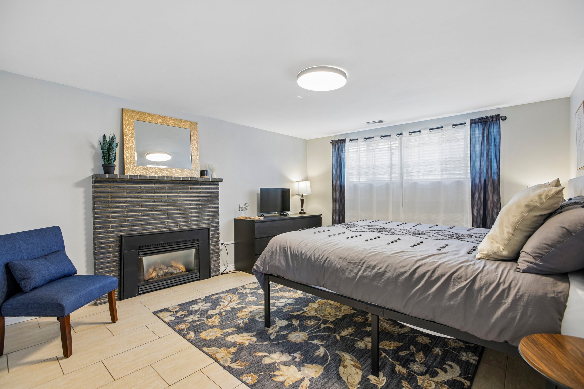 Bedroom featuring a dark brick fireplace with a black insert, light tile flooring, and a flush-mount ceiling light
