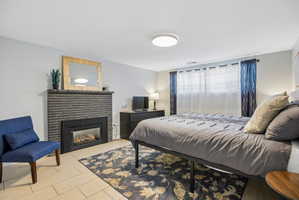 Bedroom featuring a dark brick fireplace with a black insert, light tile flooring, and a flush-mount ceiling light