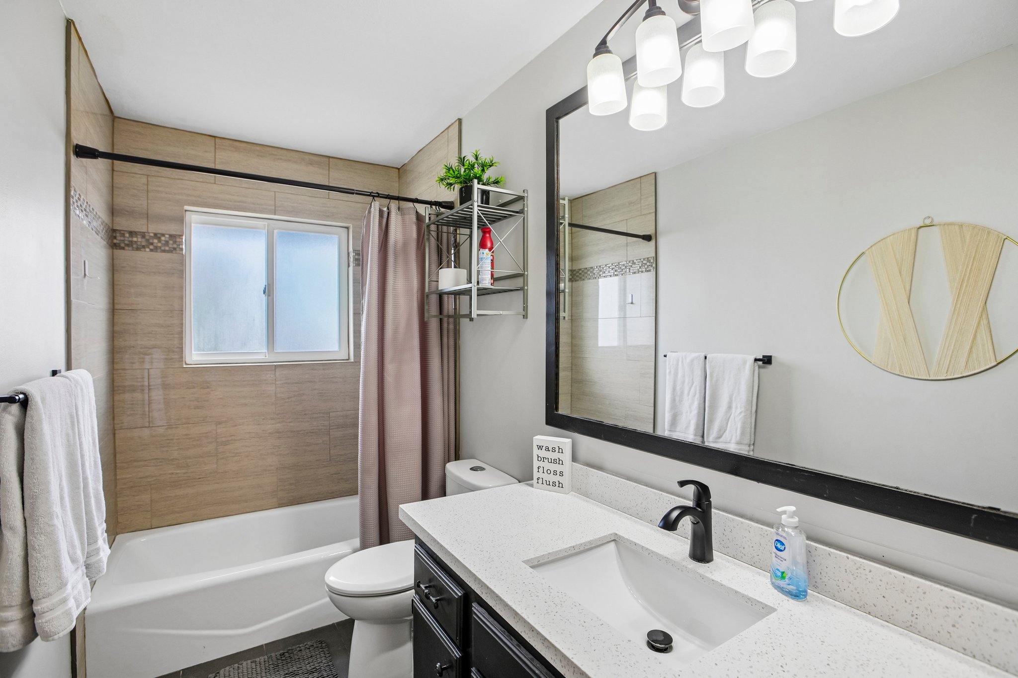 Bathroom featuring a white tub, light-colored tile surround with decorative accent band, and a white framed window