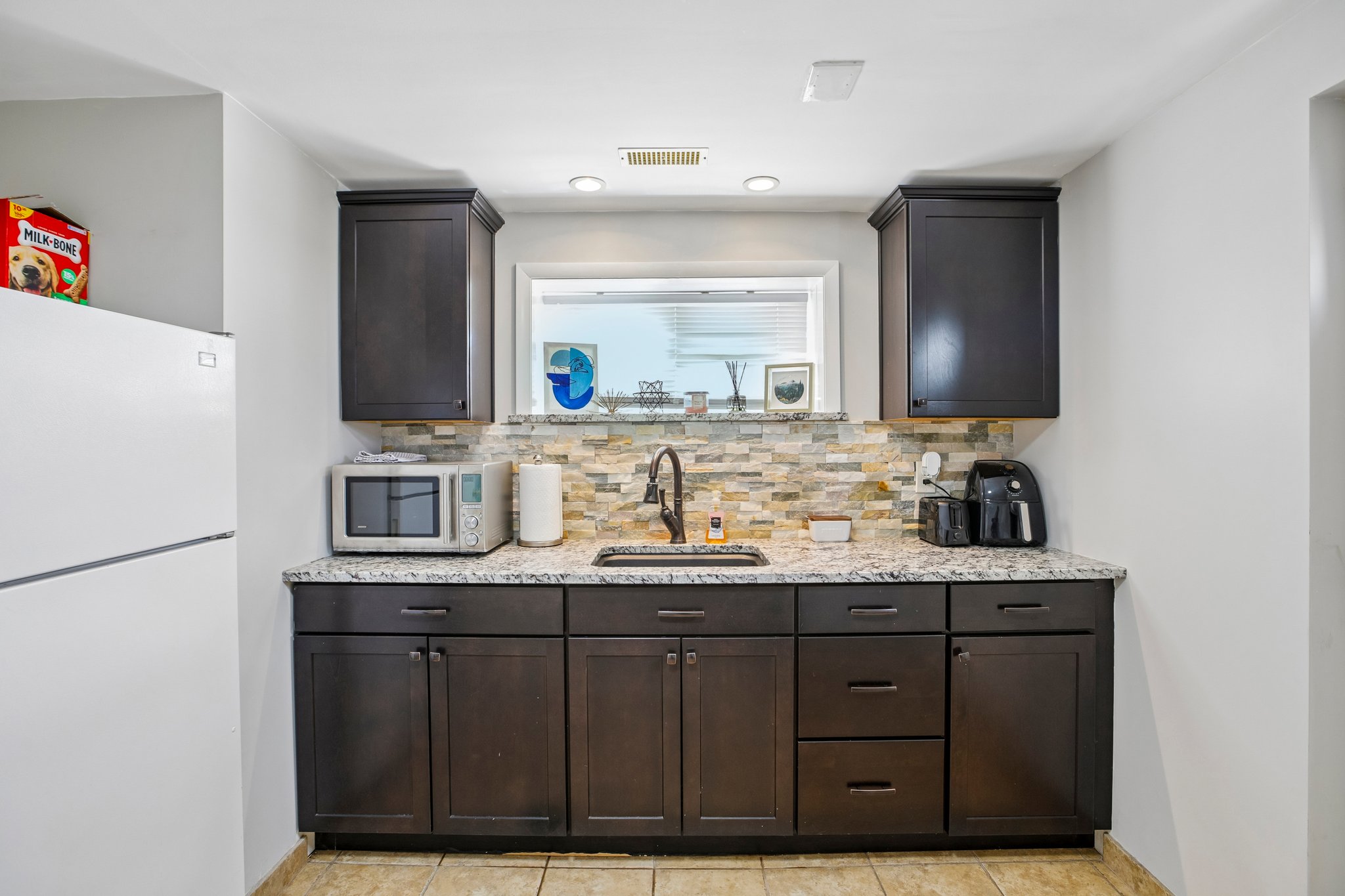 Kitchenette featuring dark wood cabinetry, a granite-finish countertop, and a stacked stone backsplash