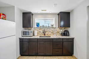 Kitchenette featuring dark wood cabinetry, a granite-finish countertop, and a stacked stone backsplash