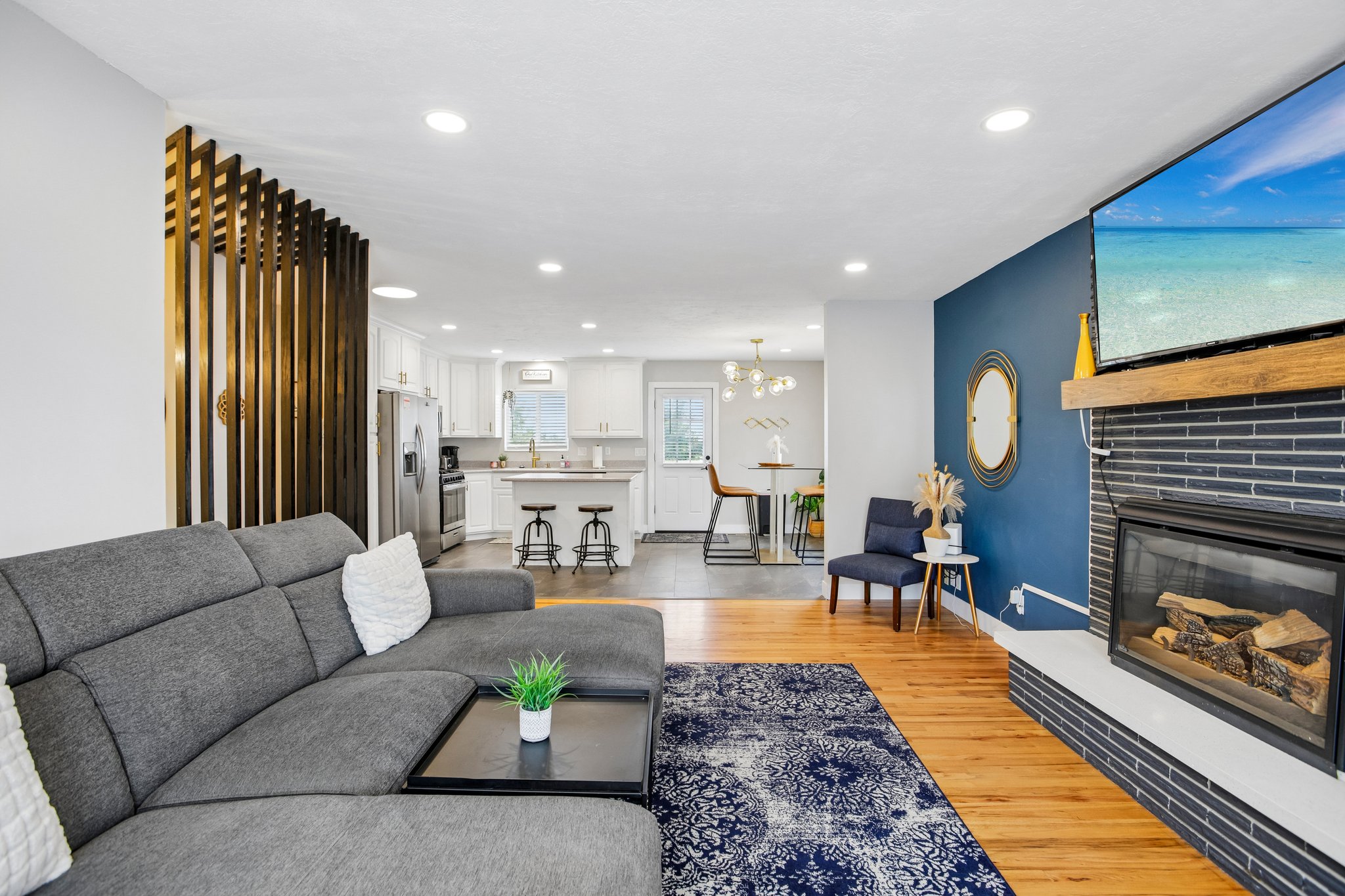 Living area featuring wood-finish flooring, a contemporary fireplace with horizontal tile surround, a wood mantel, and recessed lighting