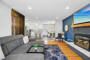 Living area featuring wood-finish flooring, a contemporary fireplace with horizontal tile surround, a wood mantel, and recessed lighting