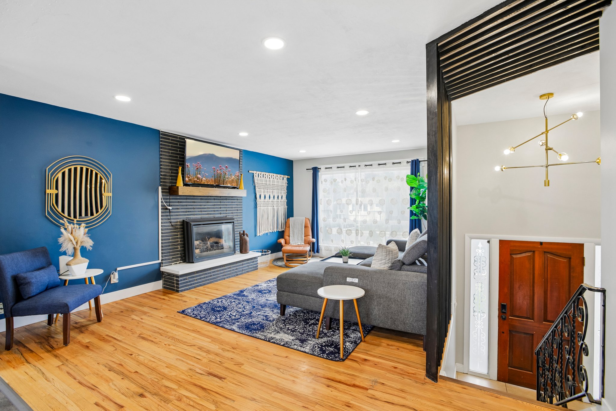 Living area featuring wood-finish flooring, a fireplace with a stone surround and hearth, recessed lighting, and a modern chandelier