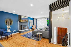 Living area featuring wood-finish flooring, a fireplace with a stone surround and hearth, recessed lighting, and a modern chandelier