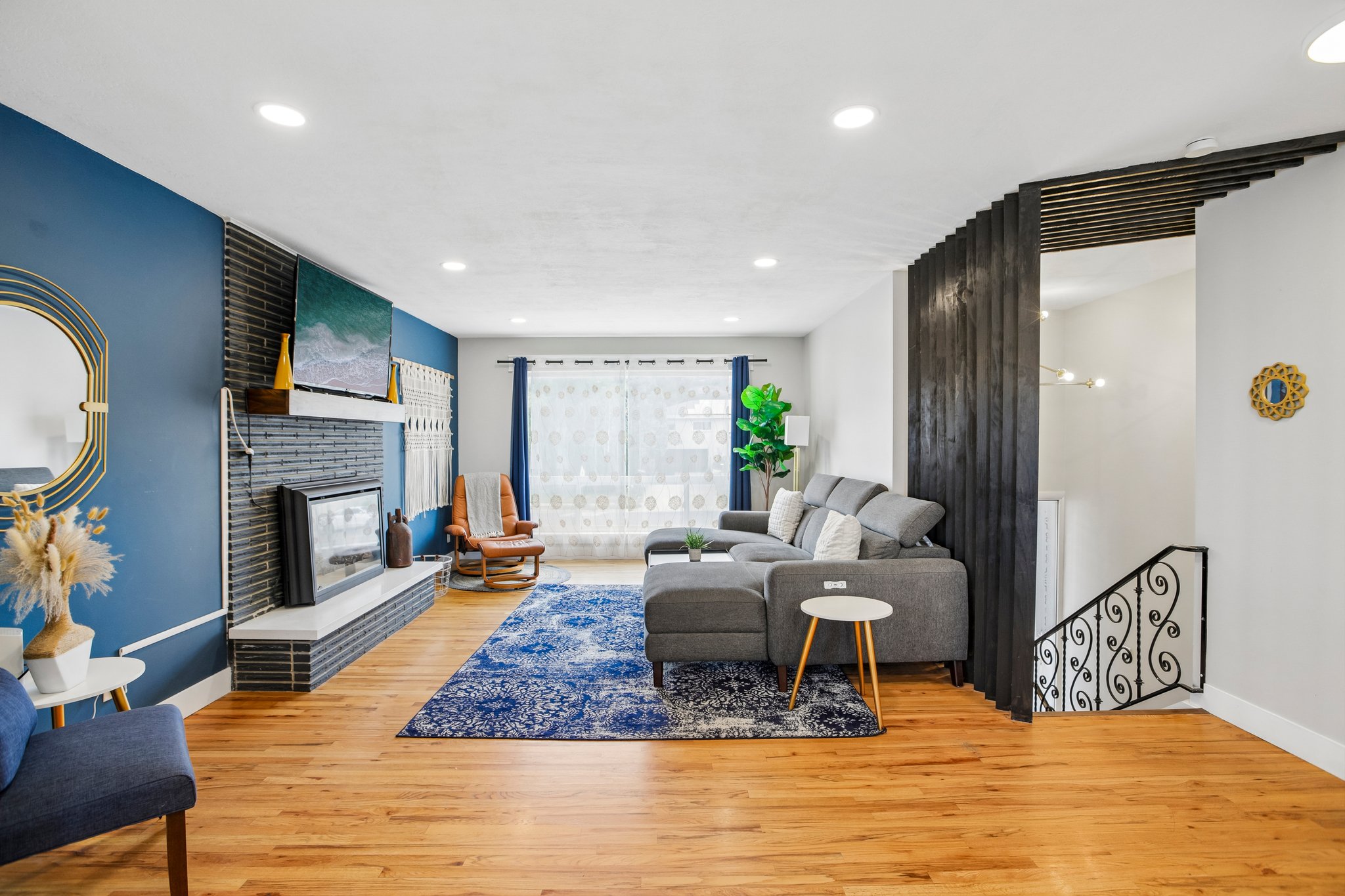Spacious living area featuring light wood-finish flooring, recessed lighting, and a modern fireplace with a black brick surround and white hearth