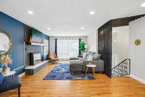 Spacious living area featuring light wood-finish flooring, recessed lighting, and a modern fireplace with a black brick surround and white hearth