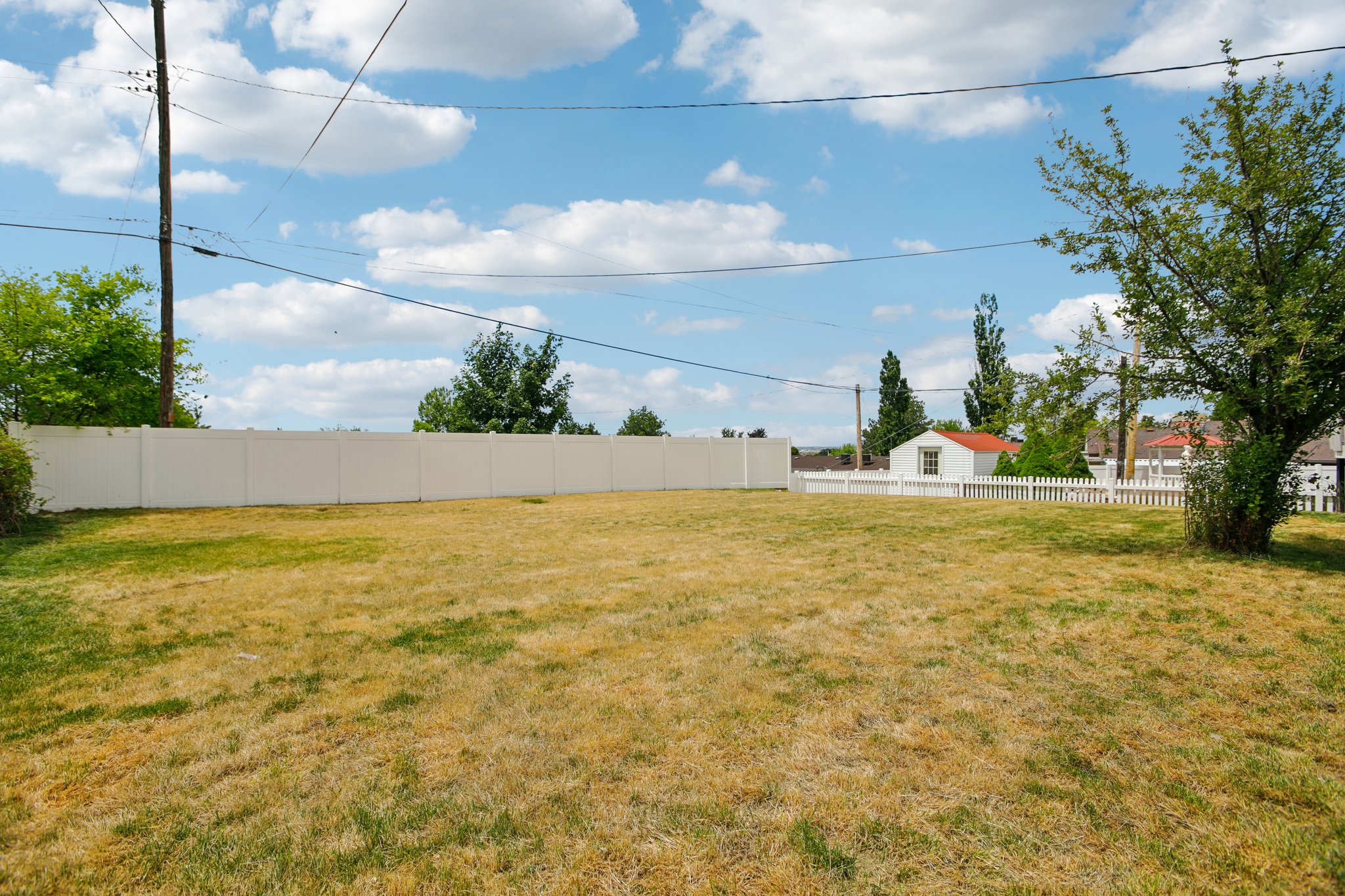 Expansive backyard featuring a large grassy area, a privacy fence along one side, and a traditional white picket fence on another