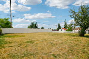 Expansive backyard featuring a large grassy area, a privacy fence along one side, and a traditional white picket fence on another