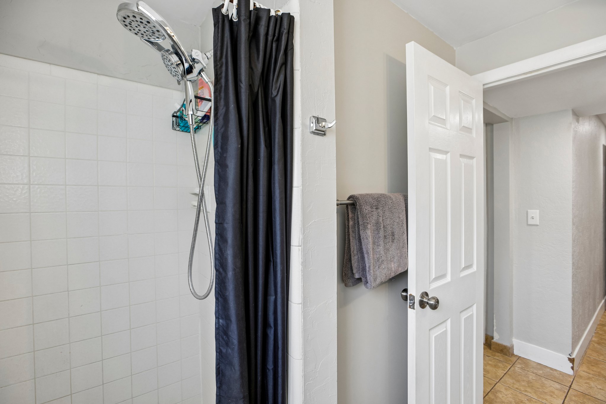 Bathroom featuring white square wall tiling, a chrome shower fixture with handheld sprayer, a panel door, and a towel bar