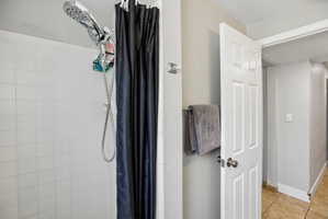 Bathroom featuring white square wall tiling, a chrome shower fixture with handheld sprayer, a panel door, and a towel bar