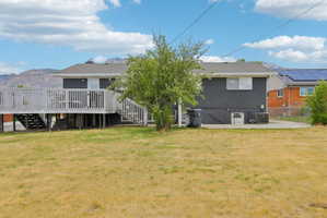 Spacious rear yard featuring an elevated deck with white railing, a mature tree, and a concrete patio