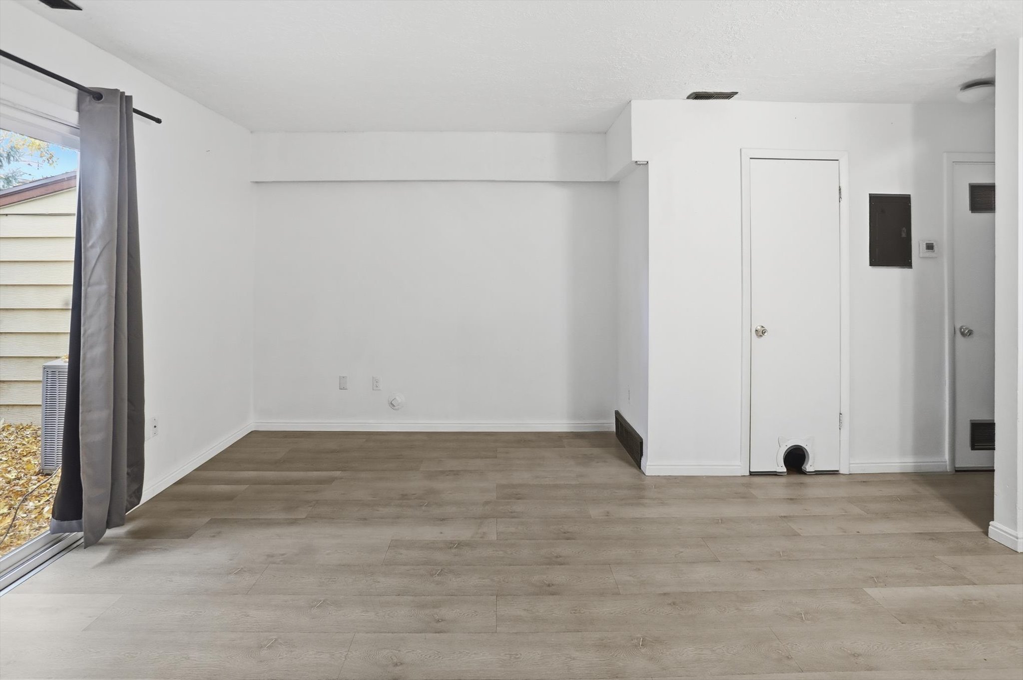 Spacious room featuring light wood-finish flooring, white walls, and a sliding glass patio door