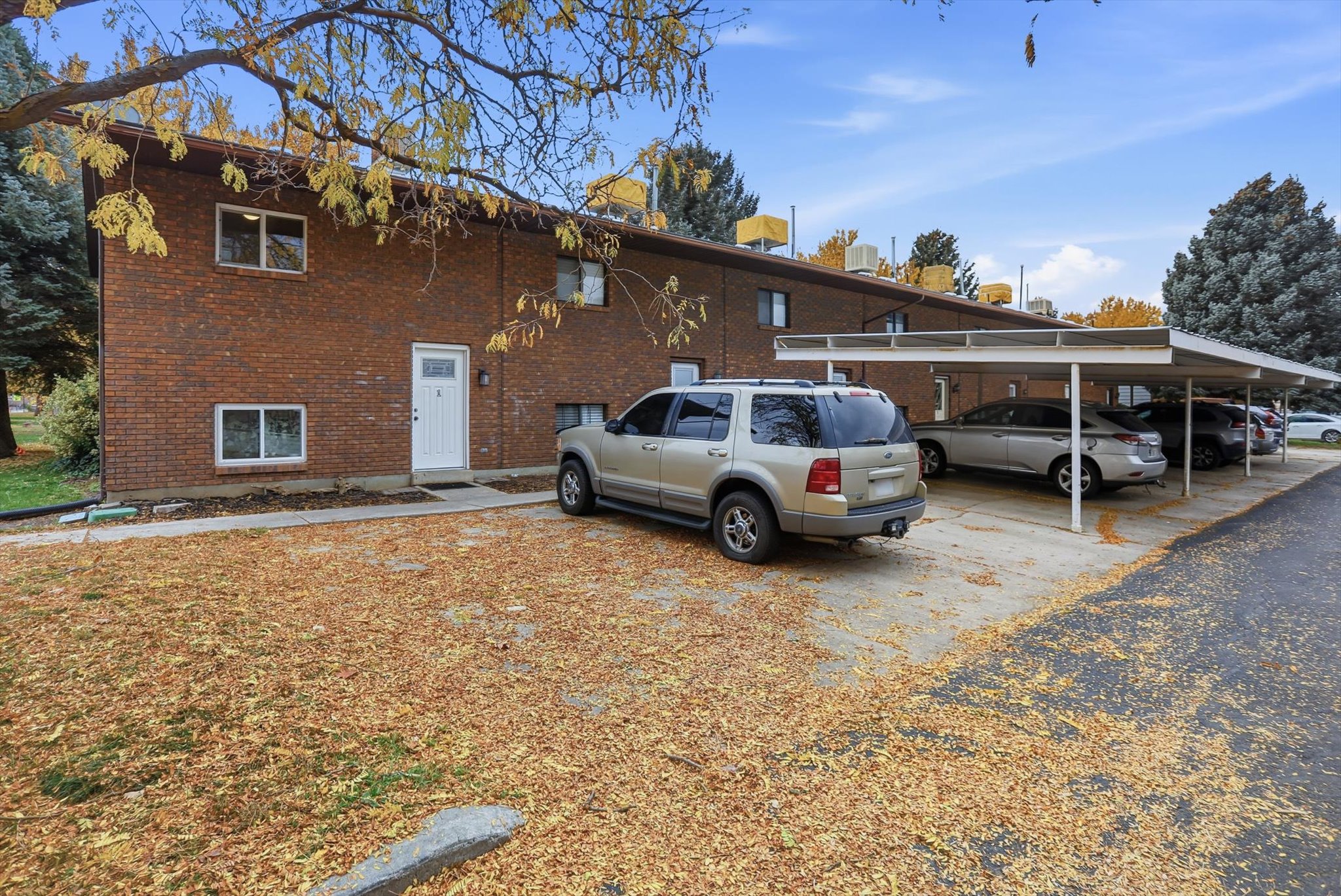 Brick exterior building featuring a white entry door, multiple windows, and covered parking structures