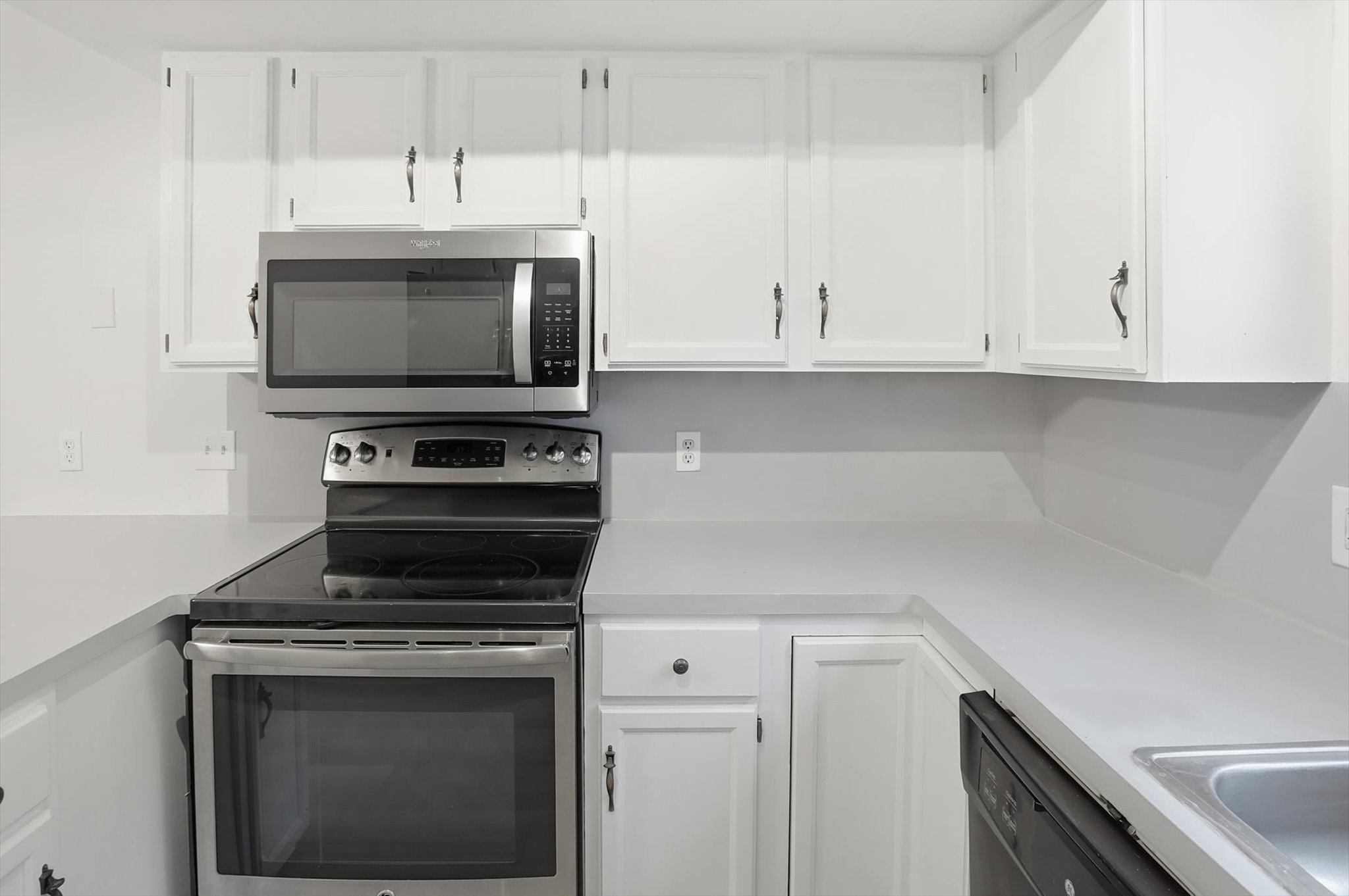 Kitchen featuring white cabinetry, light countertops, stainless steel microwave, electric range with a black ceramic cooktop, and a stainless steel sink