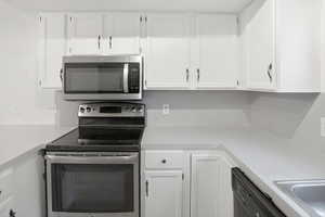 Kitchen featuring white cabinetry, light countertops, stainless steel microwave, electric range with a black ceramic cooktop, and a stainless steel sink
