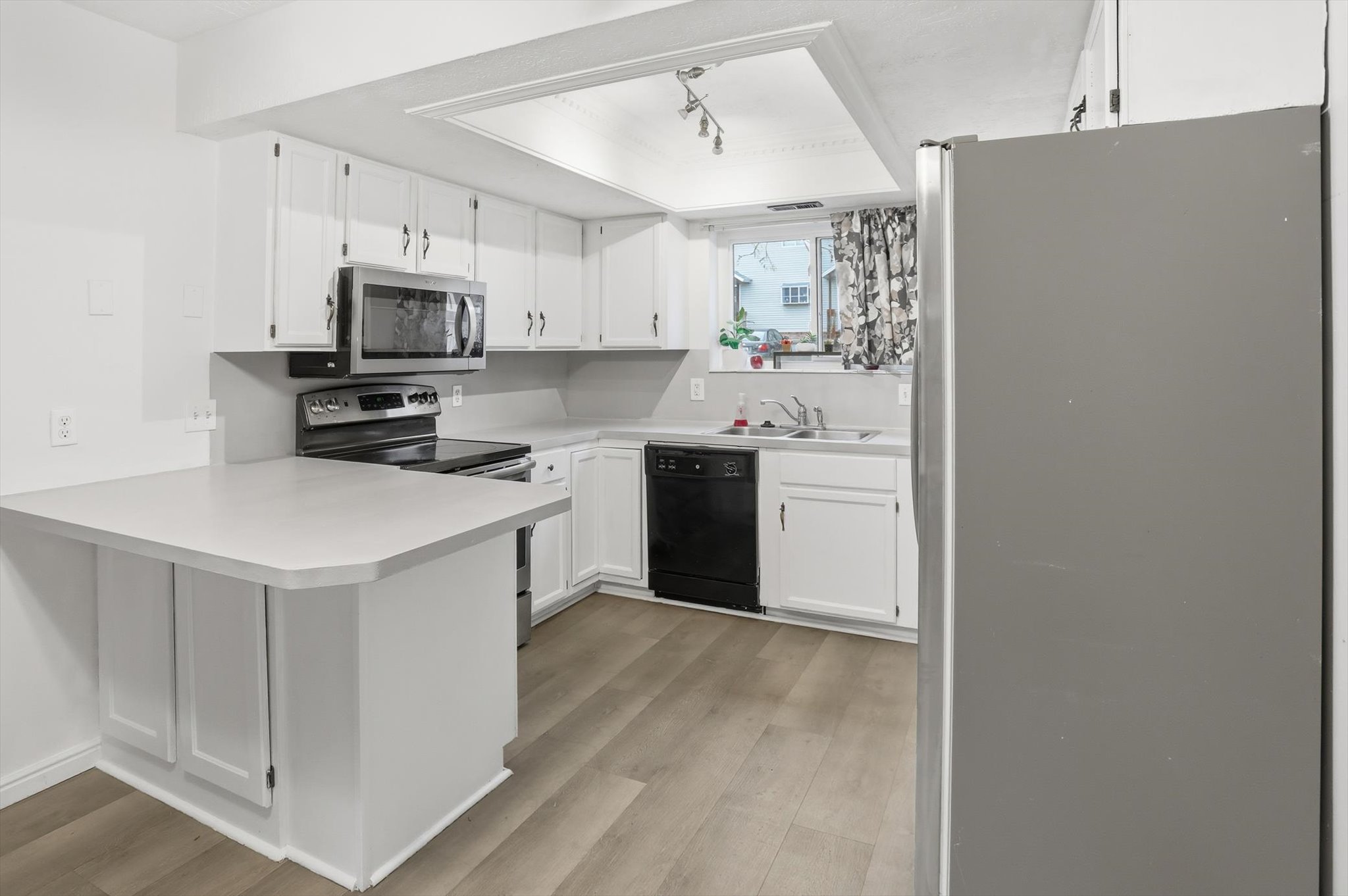 Kitchen featuring wood-finish flooring, white cabinetry with silver hardware, gray countertops, and stainless steel appliances including a microwave, range, and refrigerator