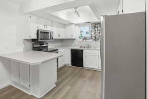 Kitchen featuring wood-finish flooring, white cabinetry with silver hardware, gray countertops, and stainless steel appliances including a microwave, range, and refrigerator